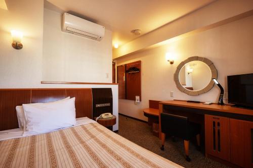 a hotel room with a bed and a desk and a mirror at GRG Hotel Naha Higashimachi in Naha