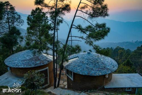 two buildings with trees and a sunset in the background at Sukoon Nature Retreat Near Bhatrojkhan Ranikhet in Tota Ām