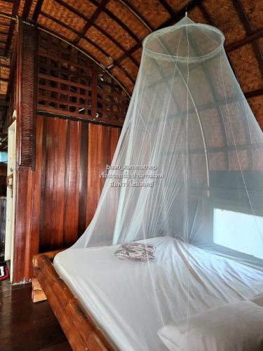 a bed with a mosquito net hanging over it at p2 เรือนกระท่อมน้ำ เรือนรอยน้ำ บ้านกามเทพ อัมพวา โฮมสเตย์ in Amphawa