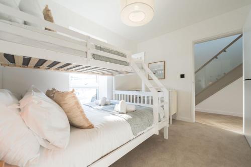 a white bedroom with a bunk bed and a staircase at Tai Porth Llechog Townhouse By Birch Stays in Amlwch