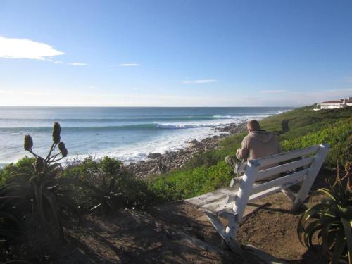 Un uomo seduto su una panchina che guarda l'oceano di Modern Holiday Home by the Sea a St Francis Bay