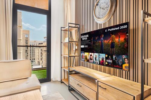 1BR Apartment With Balcony - 9 Mins to Sharjah Airport - Balcony Breeze في الشارقة: غرفة معيشة مع تلفزيون وساعة على الحائط