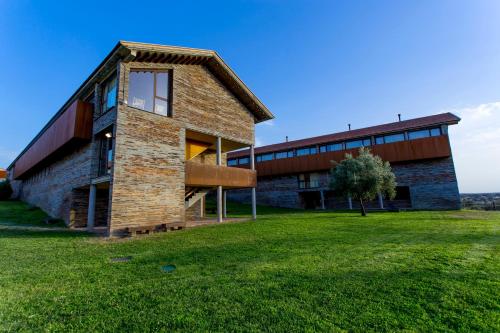 un edificio de ladrillo con un campo de hierba delante de él en Hotel Parque de Monfragüe, en Torrejón el Rubio