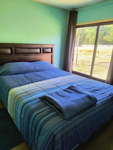 a bedroom with a bed with a blue blanket and a window at Casa entré Fundos in Lago Ranco