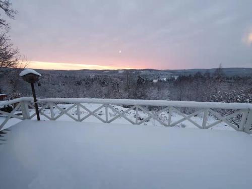 a fence covered in snow with a sunset in the background at House with beautiful lake view in Alingsås