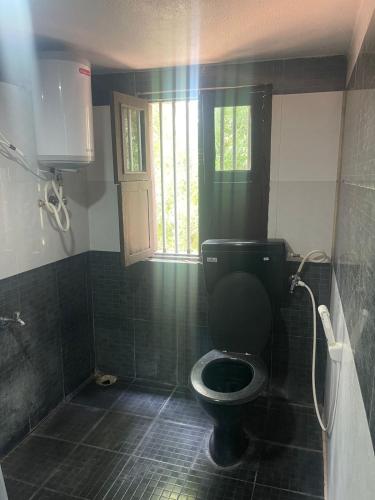 a bathroom with a black toilet and a window at Yes Yes Farms in Pollāchi