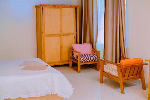 Un dormitorio con una cama y dos sillas y una ventana. en Quality Inn Motel, Nyanza, en Gahondo