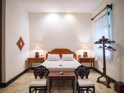a bedroom with a bed and two chairs and a table at Hotel Tugu Blitar in Blitar