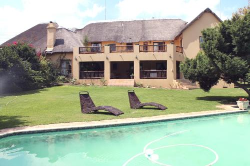 a house with two chairs in front of a swimming pool at Blue Hills Lodge in Midrand