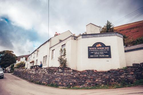 a white house with a sign on a stone wall at The White Horse Inn Bunkhouse in Threlkeld