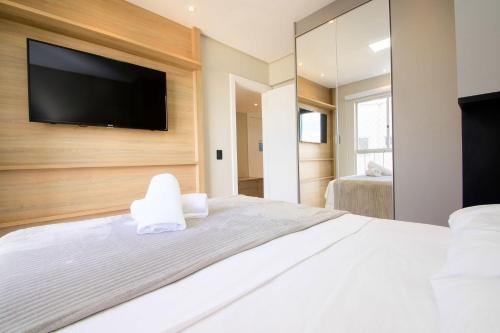 a bedroom with a white bed with a flat screen tv on a wall at Apto Vista Mar na Av. Atlântica, Barra Sul NF1414 in Balneário Camboriú