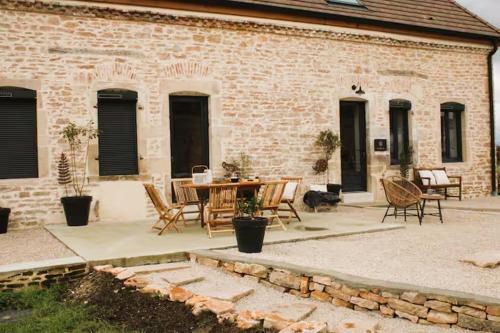 a patio with a table and chairs in front of a brick building at Les Blés Dorés et Les Graines de Lin, 2 gîtes à la Ferme avec moutons et piscine, à côté de Beaune in Corgengoux