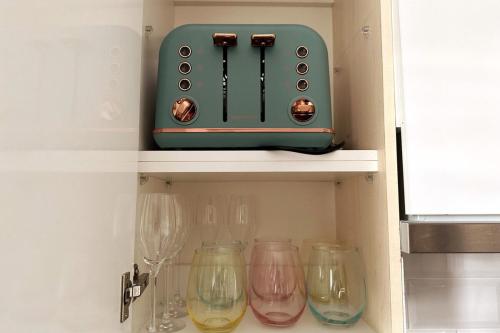 a green toaster sitting on a shelf with wine glasses at 3BR house with parking & AC, 15 mins walk to wharf in Greenwell Point