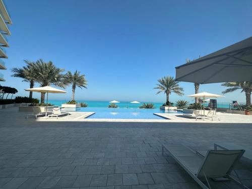 a swimming pool with chairs and umbrellas and the ocean at 2BR Soul Beach Mamsha Al Saadiyat Full Apartment in Abu Dhabi