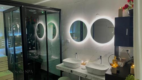 a bathroom with two sinks and mirrors on the wall at SUITE SOLIE SPA Wintzenheim in Wintzenheim