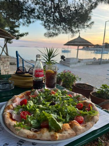 a pizza sitting on top of a table with a drink at Tessitura Murter apartman in Murter