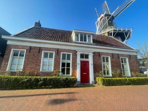 a red brick house with a windmill in the background at B&B Het Molenhuisje Winschoten - met woonkamer & keuken in Winschoten