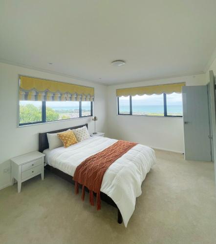 a bedroom with a large bed and two windows at Panoramic Sea & Town View Oamaru 睁眼即见太平洋 I 躺观日月同辉 in Oamaru