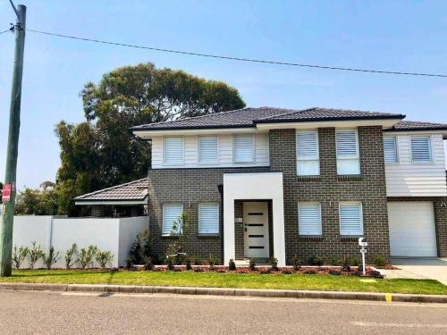 a brick house with a white fence in front of it at Family Getaway With LARGE Parent Retreat! in Shellharbour