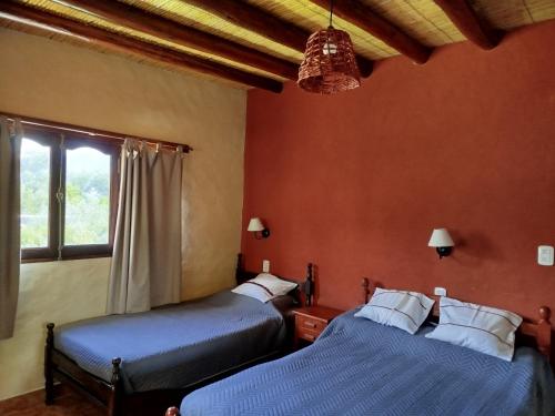 two beds in a room with orange walls and a window at La Herencia Tilcara in Tilcara