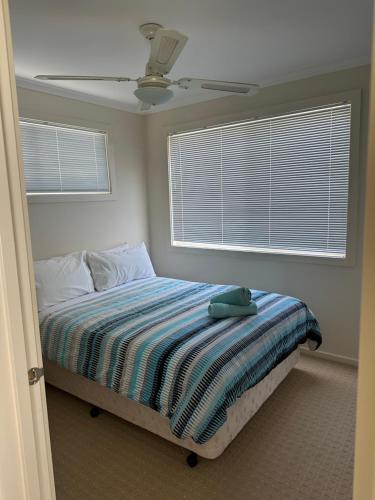 a bedroom with a bed with a striped blanket and two windows at Koonwarra Holiday Park in Lakes Entrance