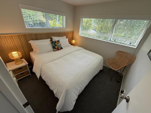 a bedroom with a bed with white sheets and two windows at Waiake Beach Apartments in Auckland