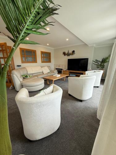 a living room with white furniture and a palm tree at Waiake Beach Apartments in Auckland