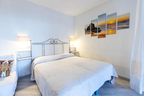 a white bedroom with a bed and paintings on the wall at Lulamax Sardegna in Budoni