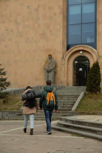 two people walking past a statue in front of a building at 11+1 by TUMO in Dilijan