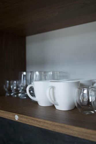 two cups and glasses sitting on a wooden shelf at Petrick House in Verkhovyna