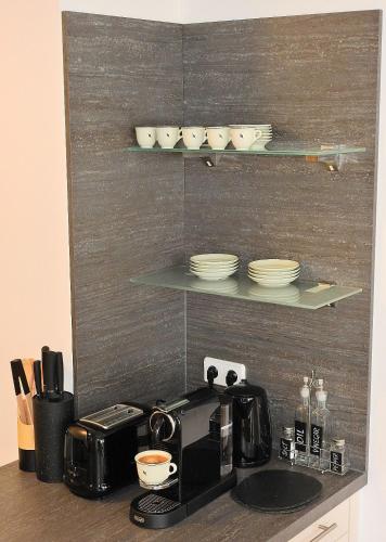 a kitchen counter with a coffee maker and cups on a shelf at Wien Schwechat Apartment Airport in Schwechat