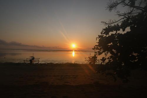 a person sitting on the beach watching the sunset at Peneeda View Beach Hotel in Sanur