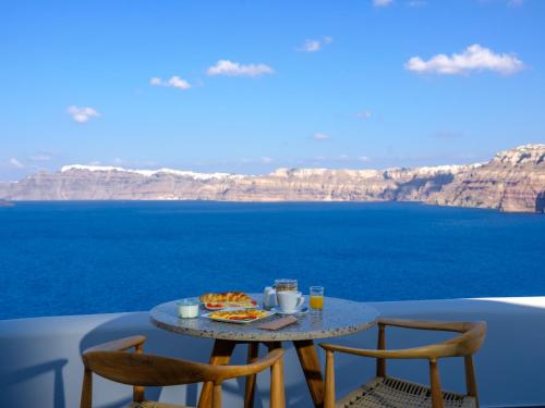 a table with food and chairs on a balcony overlooking the ocean at Neptune Luxury Suites in Akrotiri