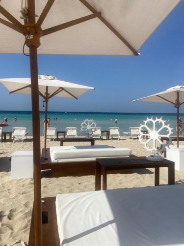 a beach with tables and umbrellas and the ocean at Masseria Messapia Wine Resort & Spa Salento in Mesagne