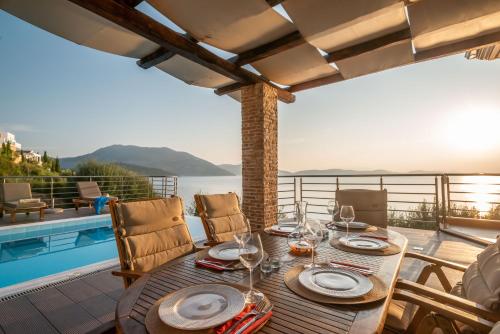 a wooden table with plates and wine glasses on a patio at Iris Villas Lefkada - Marine Villa with private sea access in Sivota