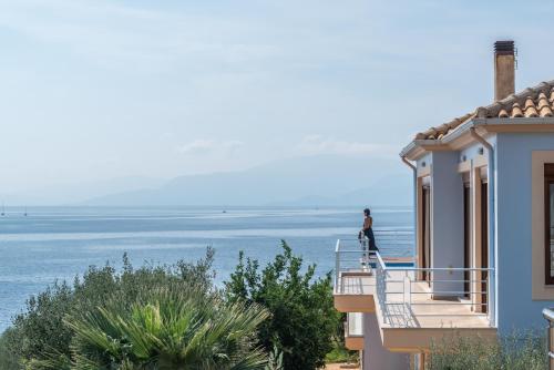 a man standing on the balcony of a house overlooking the ocean at Iris Villas Lefkada - Marine Villa with private sea access in Sivota