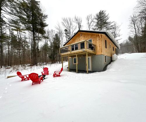 a house with two red chairs in the snow at The Mont Haus - Minutes to Mt Snow & Stratton! in Wardsboro