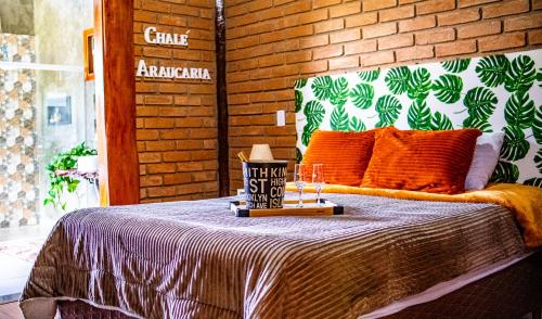 a bedroom with a bed with orange pillows and a brick wall at Chalé Araucária- Vale das Pedras MG in Sapucaí-Mirim