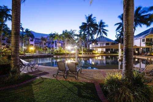 a resort pool with chairs and palm trees at night at Coral Sands Beachfront Resort in Trinity Beach