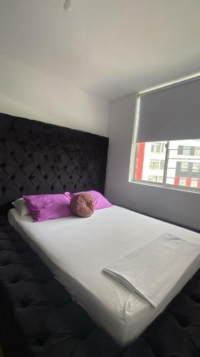 a large white bed with purple pillows and a window at David Cómodo Apartamento con Piscina in Armenia