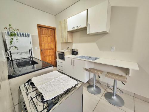 a kitchen with white cabinets and a counter with stools at Casa em condomínio in Ponta Porã