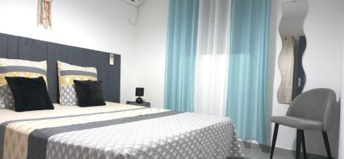 a bedroom with a bed with a chair and blue curtains at Maison Laurencia - Appartement au rez-de-chaussée avec jardin in Sainte-Anne