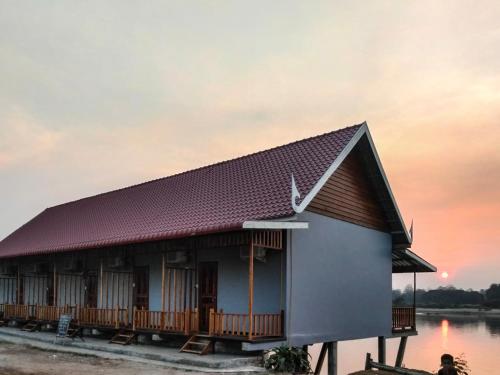 a house on the water with a sunset in the background at DODAND Studio & Sunset Riverside Guesthouse in Don Det