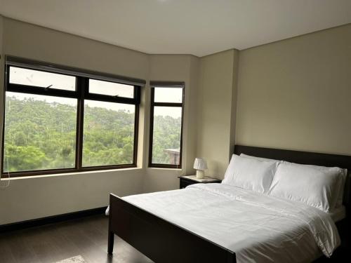 a bedroom with a large bed and two windows at Crosswinds Nature View Suite in Tagaytay