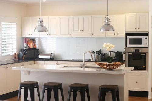 a kitchen with white cabinets and a counter with stools at Beautiful Home Away From Home in Bowral in Bowral