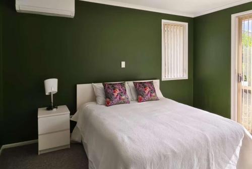 a bedroom with green walls and a bed with pillows at Hamilton East Haven in Hamilton