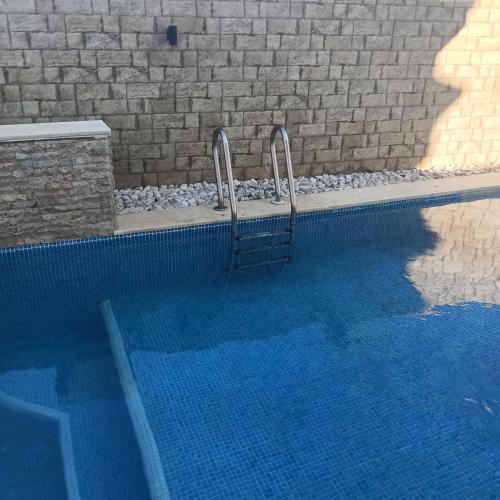 a blue swimming pool with two metal stairs next to a brick wall at Relaxing Villa with pool in El Haouaria