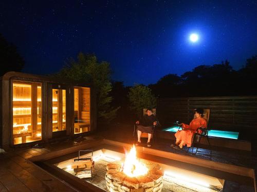 two people sitting around a fire pit at night at saunea白州 in Hokuto