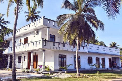 a white building with palm trees in front of it at Eco Rich Villa in Pamunugama
