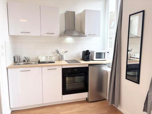 une cuisine avec des armoires blanches, un évier et une cuisinière dans l'établissement Grand studio pour 2 voyageurs - Hypercentre, à Roubaix